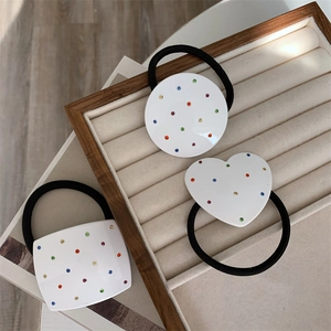 Close-up of three white resin hair ties with colorful rhinestones on a wooden tray