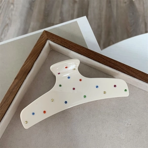 Close-up of cream acetate hair claw clip with colorful rhinestones on a wooden tray