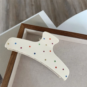 Detail of cream hair claw clip with colorful rhinestones on grey velvet display tray