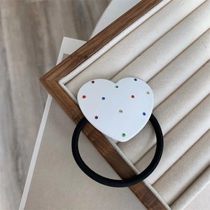 Detail of heart hair tie with colorful crystals on a wooden jewelry display stand