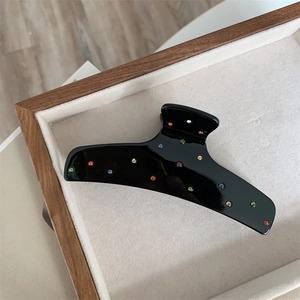 Detail view of large black acetate hair claw with colorful rhinestones on wood tray