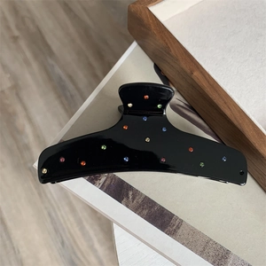Close-up of black acetate hair claw clip with colorful rhinestones on a wooden tray