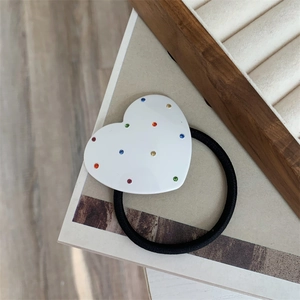 Detailed view of black elastic hair tie featuring a white heart charm with colorful rhinestones