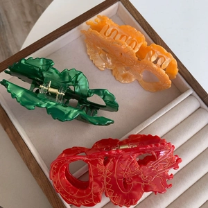 Detail van drie grote draken haarklemmen in groen, oranje en rood op een fluwelen tray