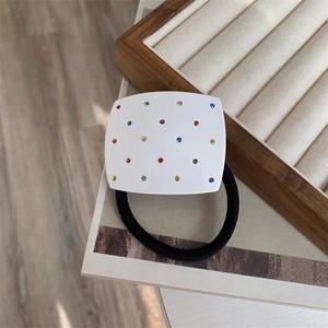 Close-up of a white square hair tie with colorful rhinestones on a wooden jewelry box
