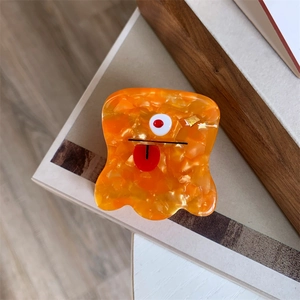 Detail of a cartoon orange monster hair claw clip with a single eye and red tongue detail