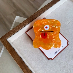 Macro shot of an orange acetate hair claw clip featuring a funny monster face with a red tongue