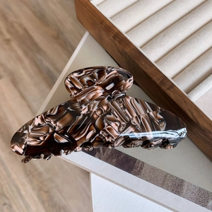 Detailed view of large tortoiseshell acetate claw clip with marble texture on wooden tray
