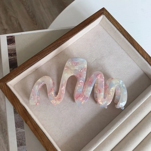 Macro detail of wave-shaped marble texture acetate hair claw clip with pearlescent finish