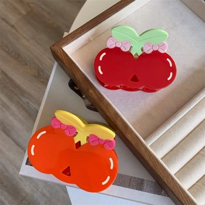 Detail of red and orange acetate cherry hair claws with cute pink bow accents in a wooden tray