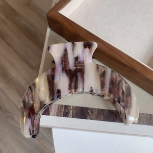 Macro shot of large crescent acetate hair claw clip with purple marble texture on wooden tray
