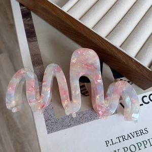 Detail of oversized marble pattern acetate hair claw clip with unique wavy s-curve design