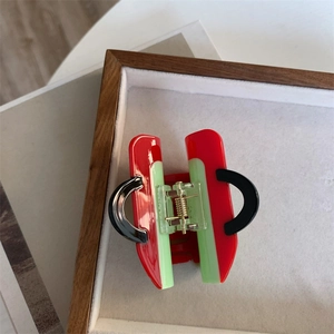 Detail view of a creative handbag-shaped hair claw in red, green, and black acetate material