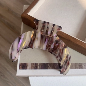 Macro detail of crescent acetate hair claw clip with artistic marble texture and metal spring