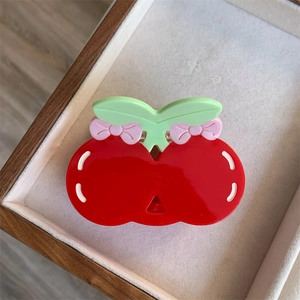 Top view of red cherry-shaped hair claw clip with green leaves in a wooden tray