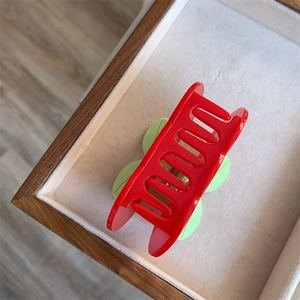 Detail of red and green acetate cherry hair claw clip on a white velvet display tray