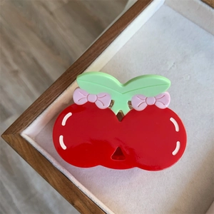 Detail of red cherry hair claw clip with green leaves and pink bow on a wooden tray
