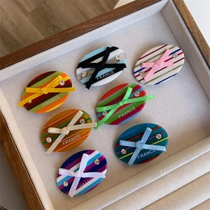 Close-up of seven acetate hair clips with colorful stripes and silk ribbon bows