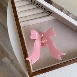 Detail view of pink acetic acid bow hair claw clip with golden metal spring on velvet