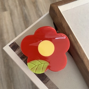 Macro detail of a glossy floral claw clip with red petals and green leaf accents