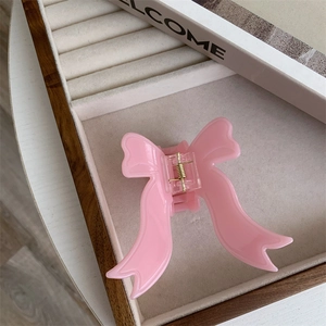Detailed view of a soft pink acetate bow hair claw clip on a beige jewelry tray