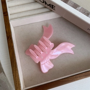 Detail of pink acetate bow hair claw clip with pearlescent finish in a jewelry tray