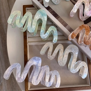 Grandes pinces à cheveux ondulées en acrylique effet marbre et perle sur un plateau