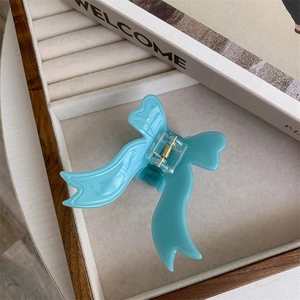 Macro detail of a light blue acetate bow claw clip with a strong gold metal spring