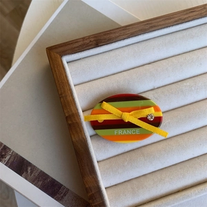Detail view of oval acetate hair clip with colorful stripes and yellow ribbon bow accent