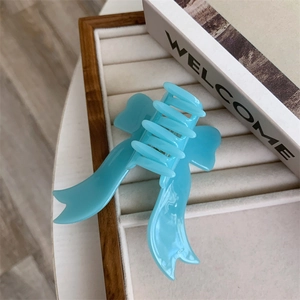 Detail view of a light blue acetate bow hair claw clip on a velvet jewelry tray