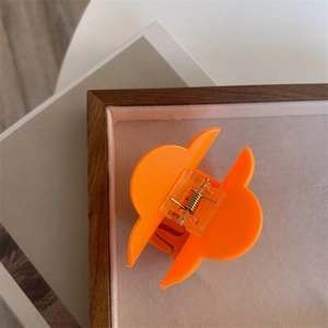 Macro detail of a bright orange flower hair claw clip on a minimalist wooden tray