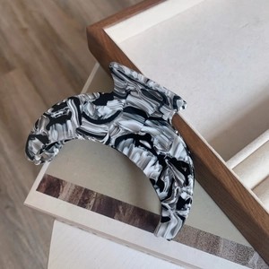 Detailed view of large black and white marble acetate hair claw clip on wooden tray