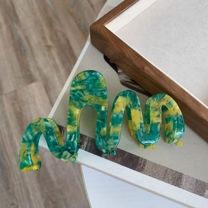 Detail of wavy acetate hair claw with green and yellow marble pattern texture
