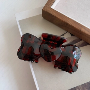Detail of red plaid pattern hair claw clip with heart design on a white book surface
