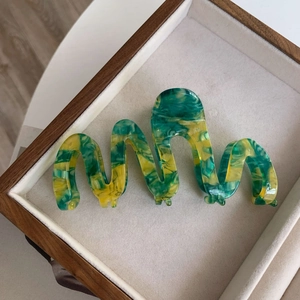 Macro detail of wave-shaped oversized hair claw in green and yellow marble acetate