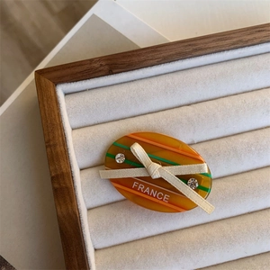 Detail showing the orange striped acetate hair clip with a white knit bow and rhinestones