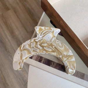 Detail of large acetate hair claw clip featuring elegant cream marble crescent design