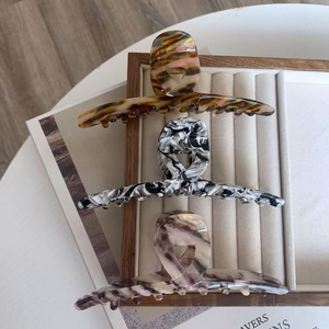 Three large acetate hair claw clips in tortoise and marble patterns on a velvet tray
