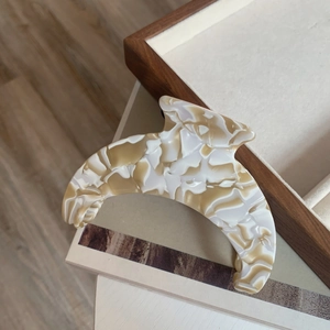 Detail of elegant crescent moon hair claw clip in beige marble acetate texture