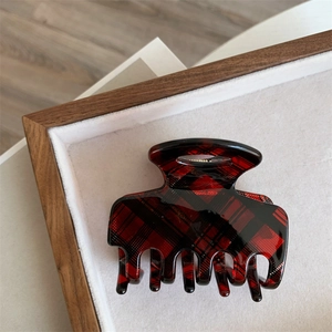 Close-up of a vintage red plaid hair claw clip on a soft velvet jewelry display tray