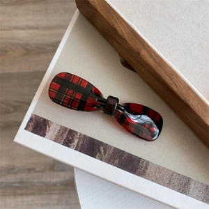 Close-up of a red plaid acetic acid hair claw with a minimalist bow design on a magazine