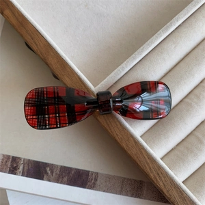 Detail of red and black plaid bow hair claw clip on beige velvet display jewelry tray