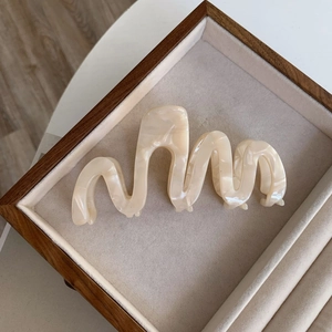 Macro shot of oversized wavy cream acetate hair claw clip with marble texture on velvet tray
