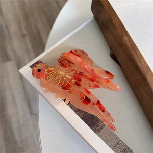 Detailed close-up of a dragonfly hair claw clip in acetate with coral tortoiseshell texture