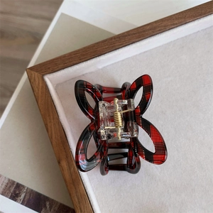 Close-up of red plaid bow hair claw clip showing glossy acetate finish and golden spring
