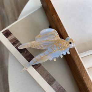 Detail of blue dragonfly hair claw clip with gold accents on a warm wooden background
