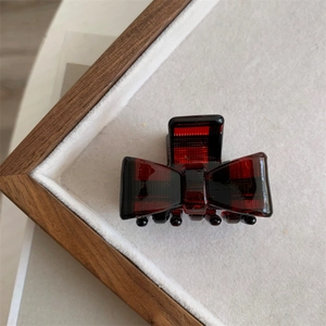 Close-up of red plaid acetate hair claw clip with bow design on velvet display tray