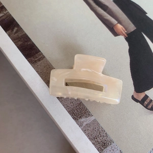 Macro shot of a cream-colored rectangular acetate hair claw on a fashion magazine background