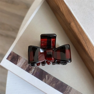 Detailed close-up of a red plaid bow hair claw clip with a glossy acetate finish