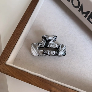 Detail view of small square acetate hair claw with monochrome marble pattern and cutout design
